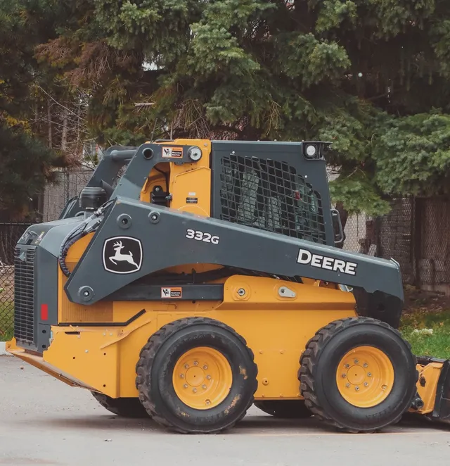 A small John Deere skidsteer sits parked outside a city jobsite.