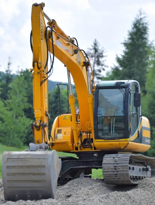 A shiny new excavator sits atop a pile of gravel with its bucket digging in.