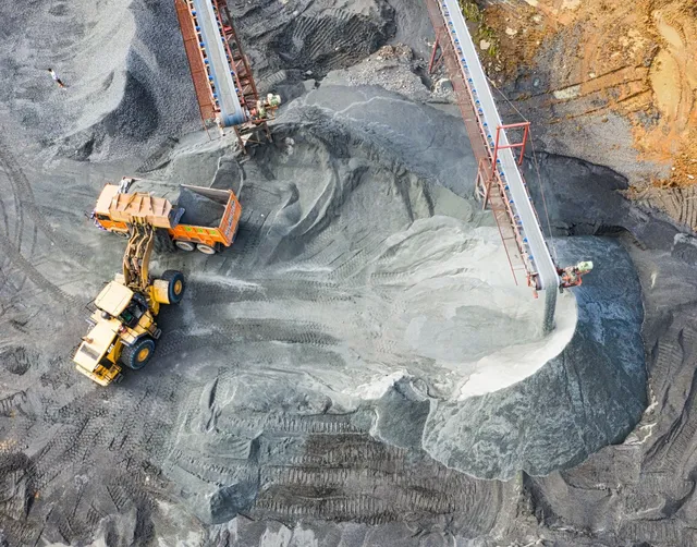 Aerial view of a large excavation site, a tractor moves gravel into the back of a dump truck.