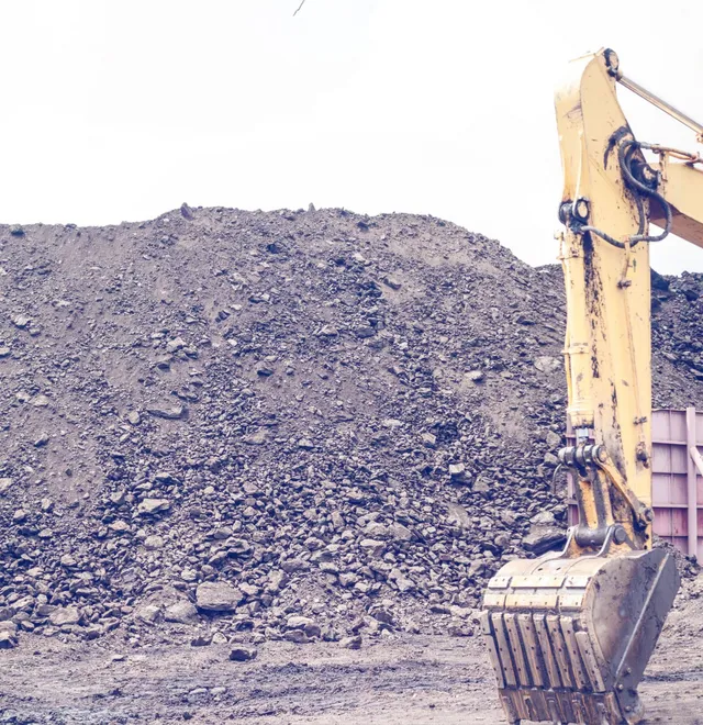 In front of a large pile of dirt and debris sits a backhoe bucket, its metal surfaces gleaming in the sunlight.