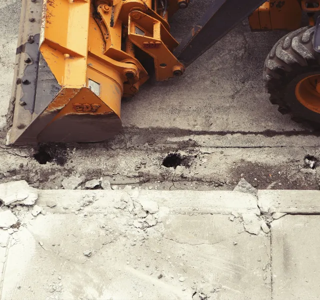 A large yellow excavation tractor parked alongside a curb, ready to get to work.