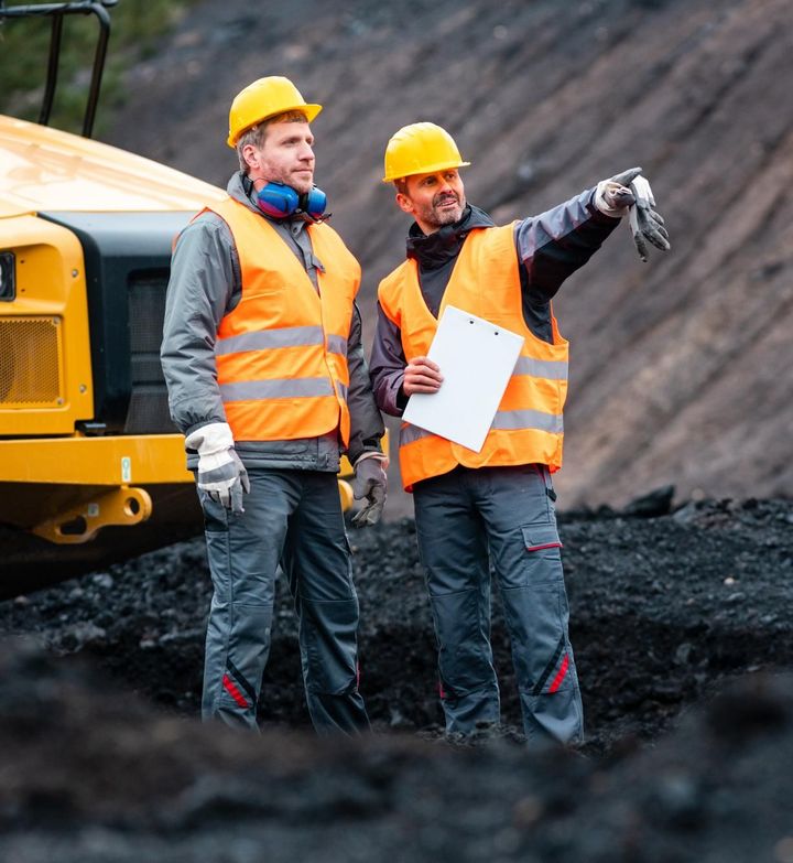 two construction workers wearing orange vests and hard hats looking at a clipboard
