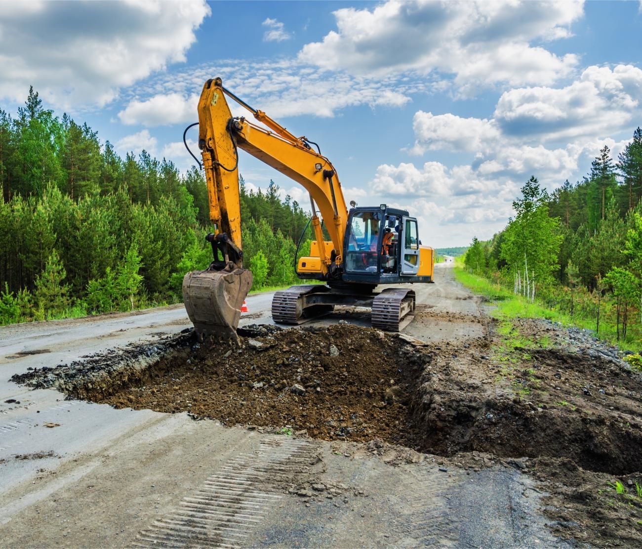a yellow excavator is digging a hole in the road