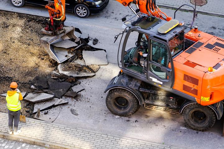 a man stands next to a large orange excavator that says ' hitachi ' on the side