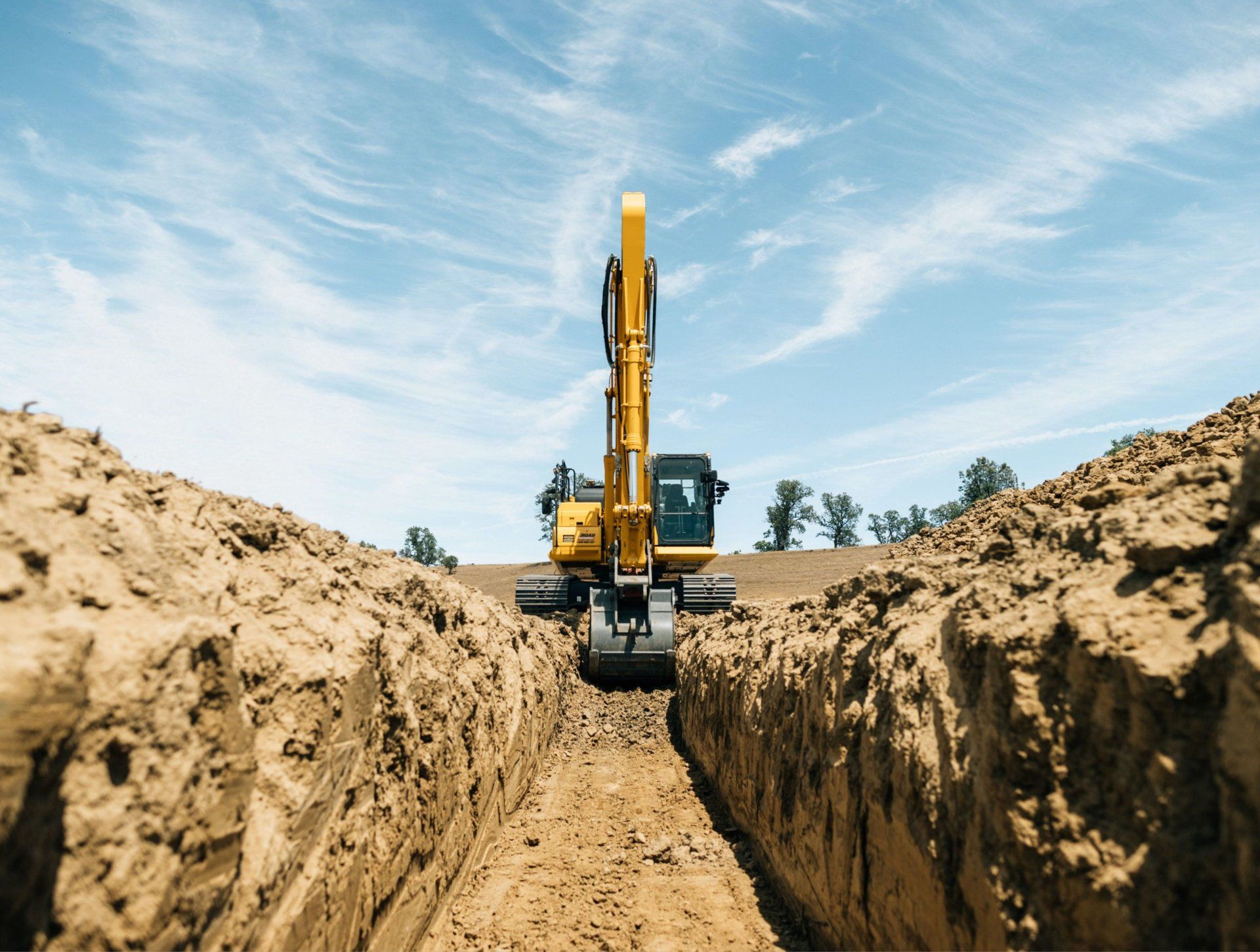 a yellow excavator is digging a trench in the dirt .
