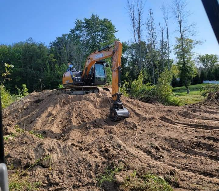 A shiny new excavator sits atop a pile of gravel with its bucket digging in.